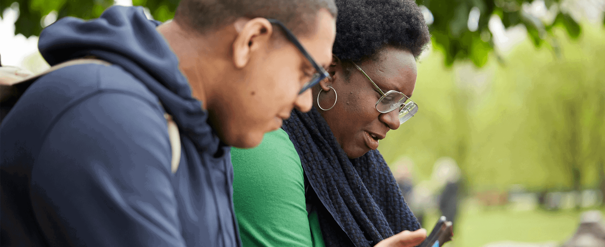 Two people sitting in a park using their mobile phones.
