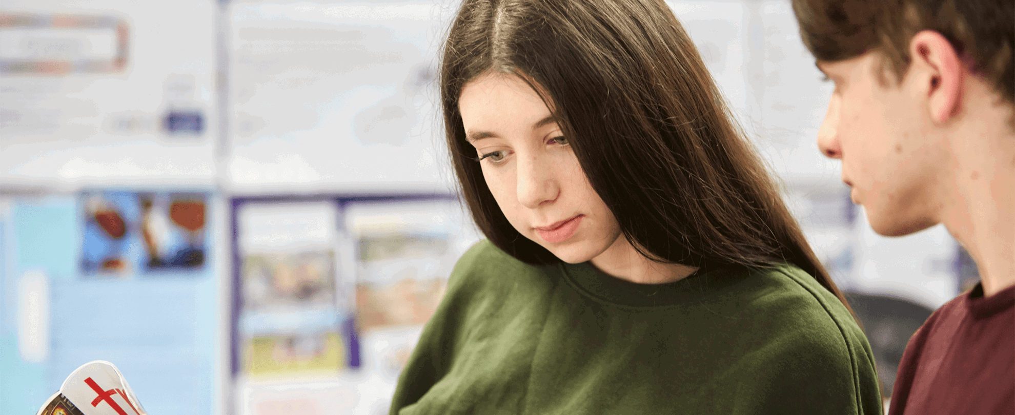 Two young people sitting in a library and reading a magazine together.