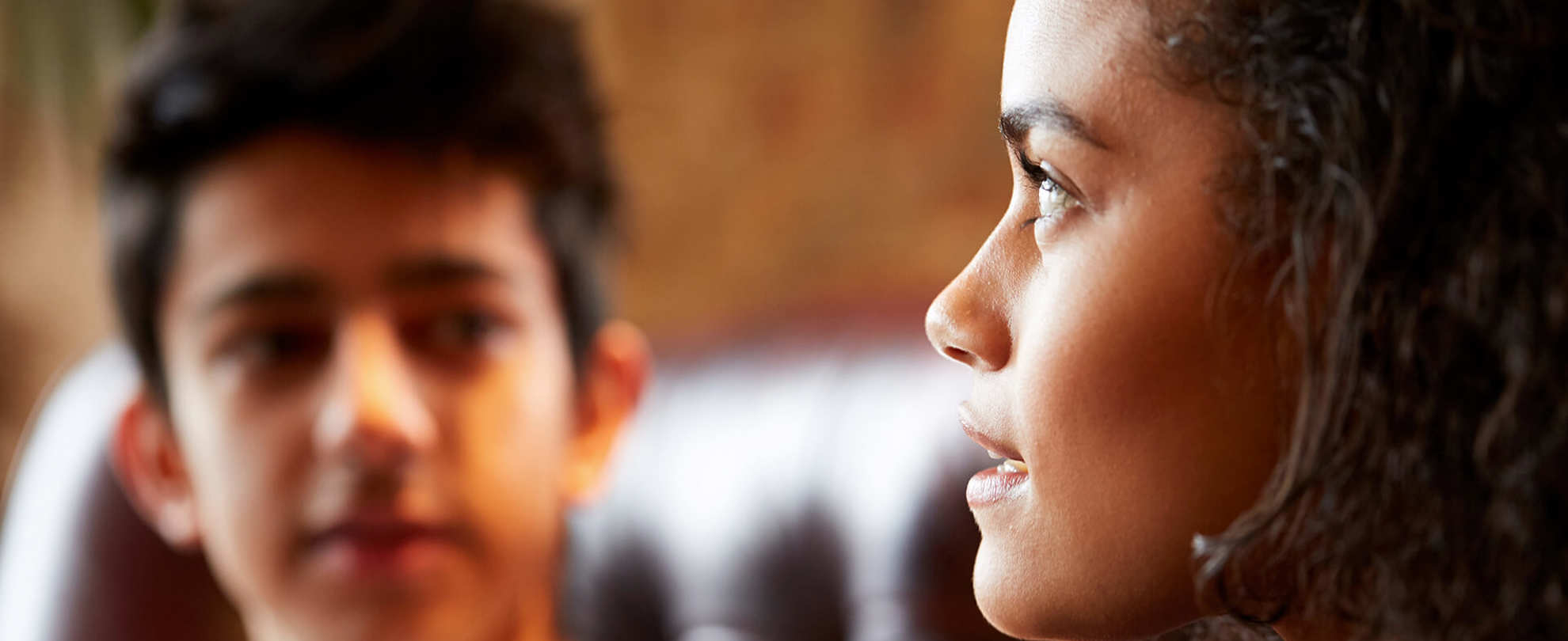 close-up-of-a-young-woman-talking-while-looking-away-and-a-young-man-on-background-looking-at-the-girl-while-she-talks