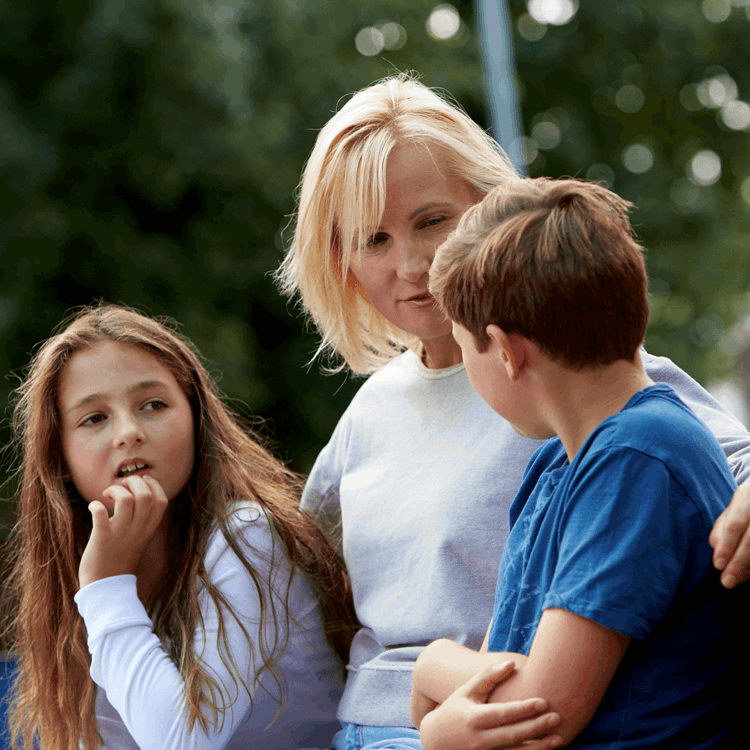 A mother sitting against a wall talking to her children with her arms around them