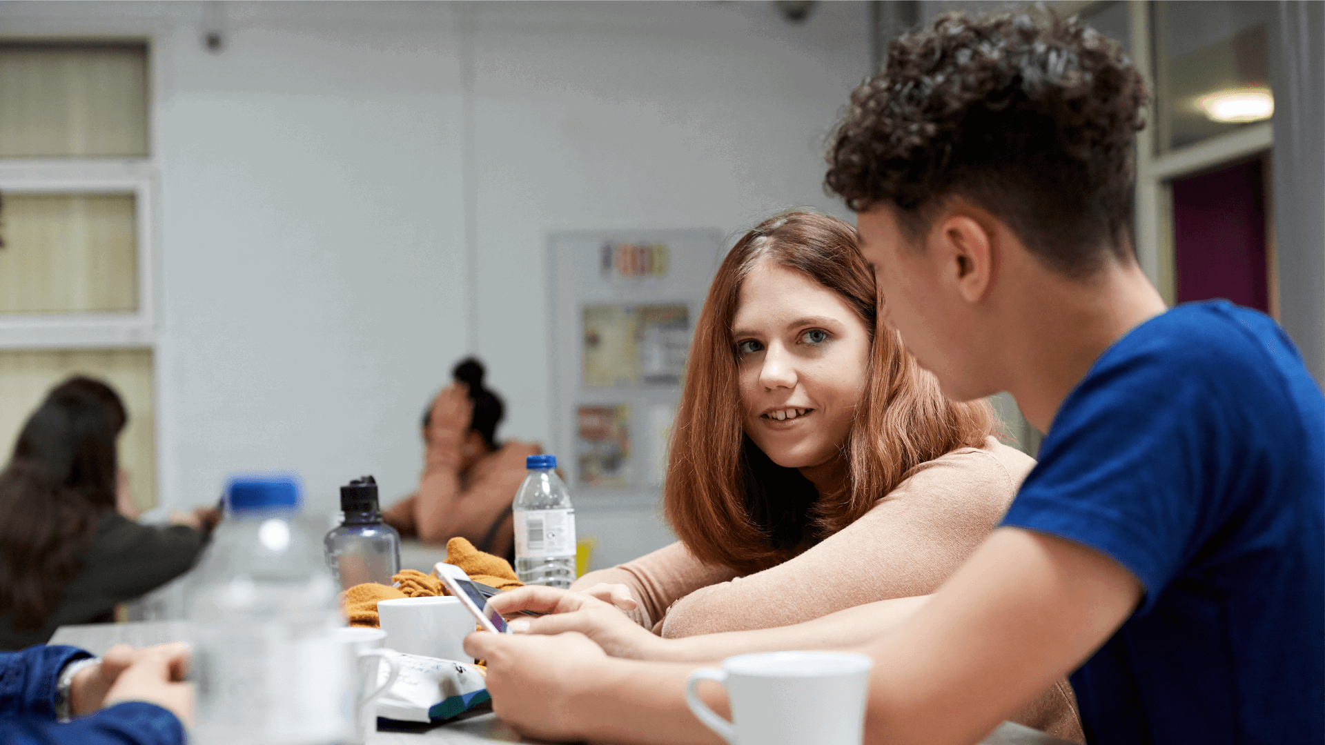 A group of young people sitting together and talking in a school canteen.