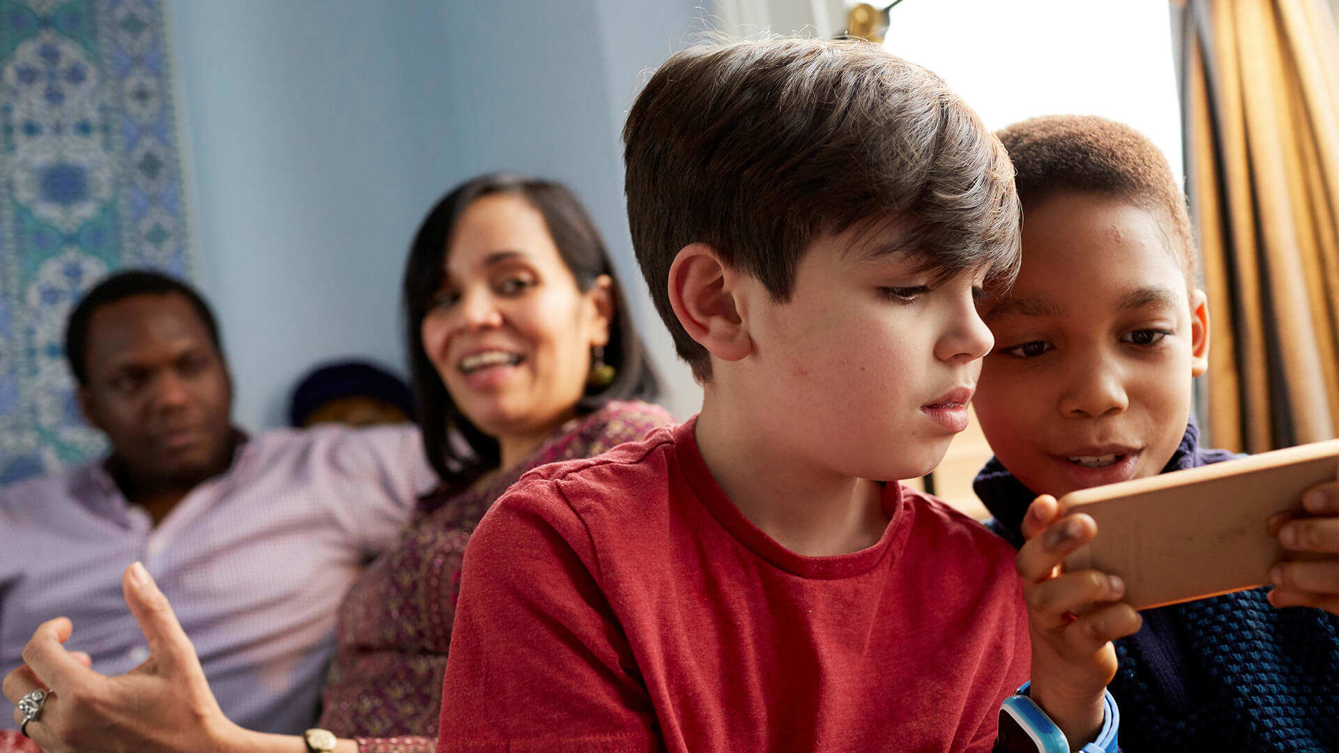 A family relaxing at home with parents chatting and children playing on a tablet
