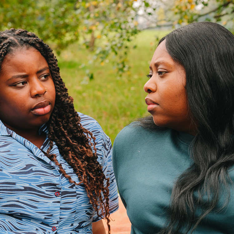 A young Black woman talking about something serious with an older Black woman in the park.