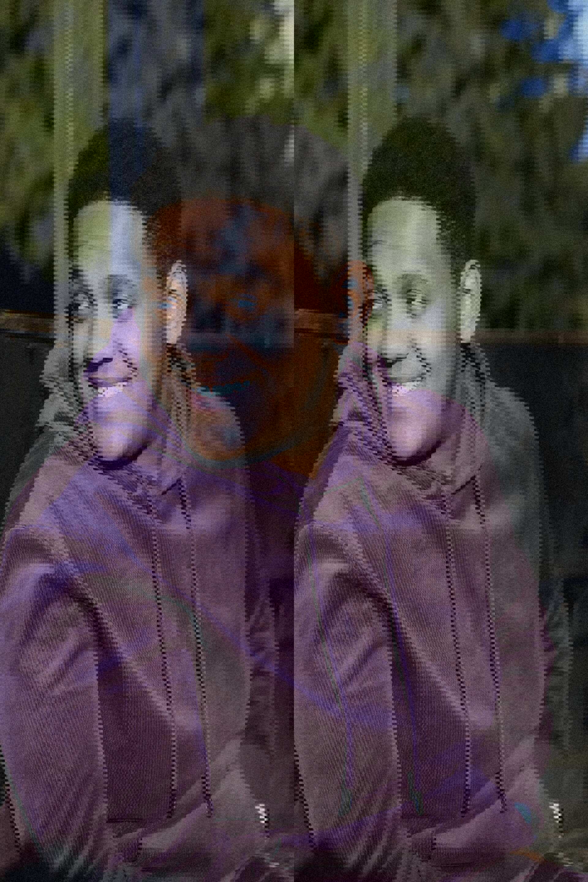 Josiah sitting in a park wearing a purple hoodie. He is looking over his right shoulder and smiling.