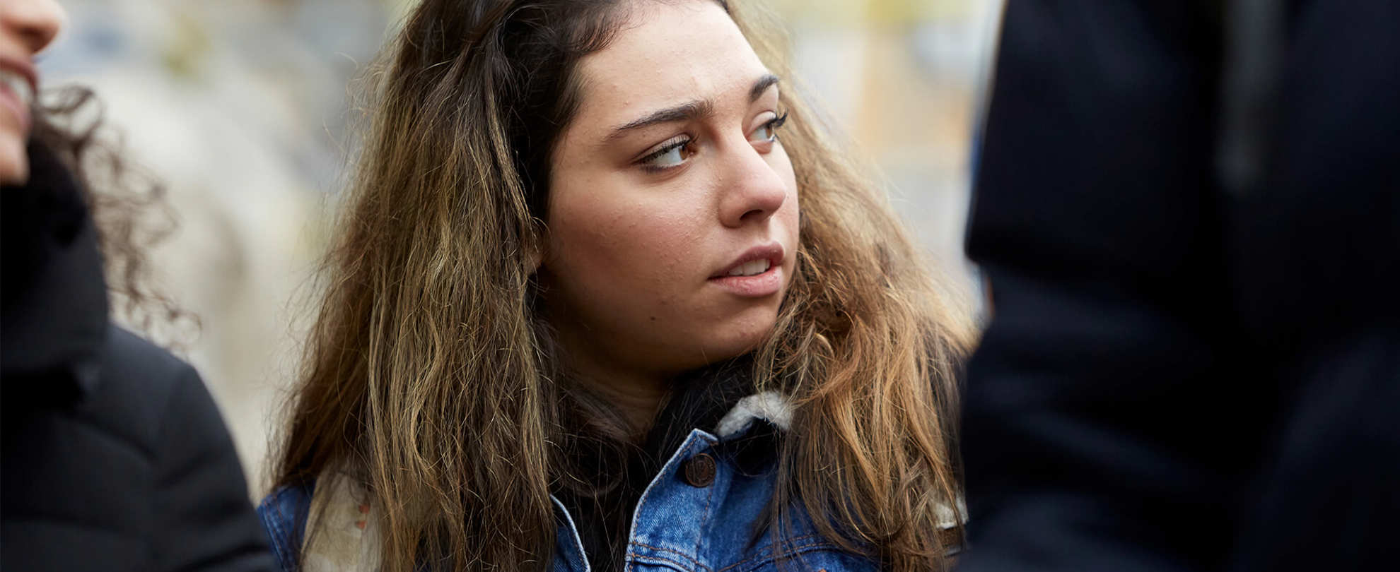 A young person looks away while she stands between two other young people.