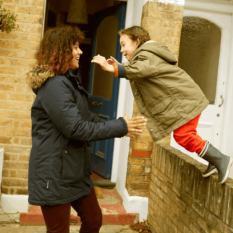 A child jumping off a wall and her mum is ready to catch her.