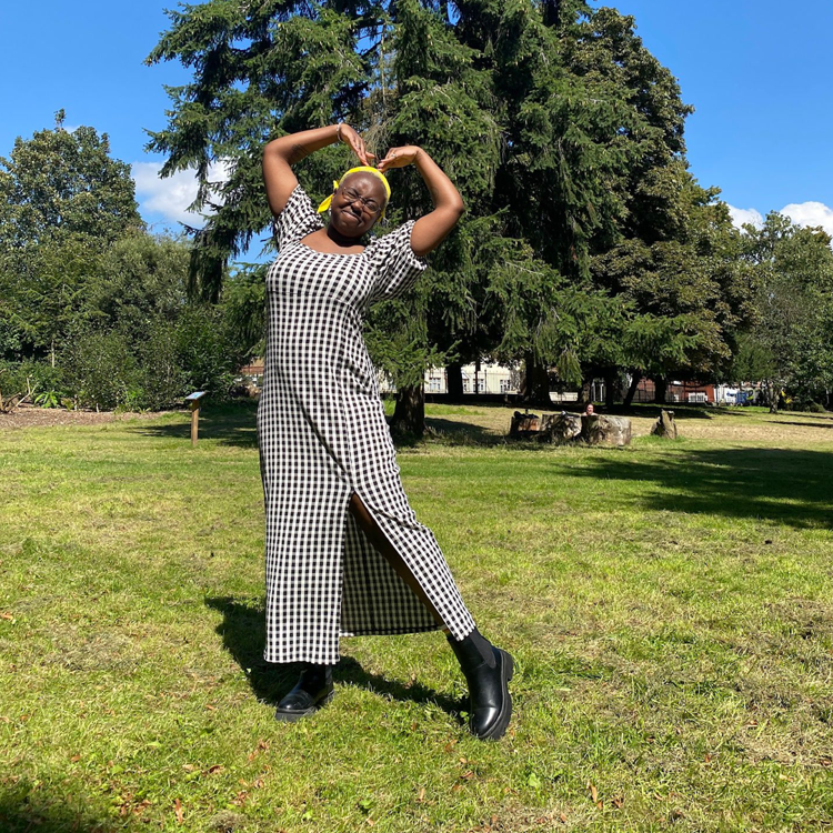 Jaleel is in a park in front of a big green tree. They have positioned their arms to create a heart shape.