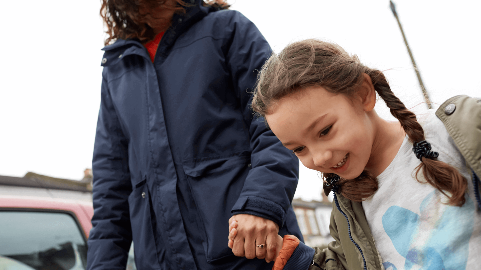 A smiling young girl is holding hands with her mum while walking in the street