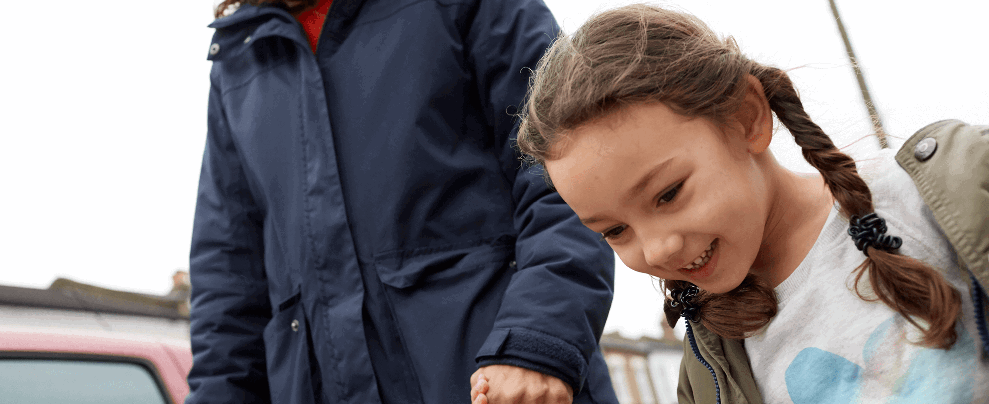 A smiling young girl is holding hands with her mum while walking in the street