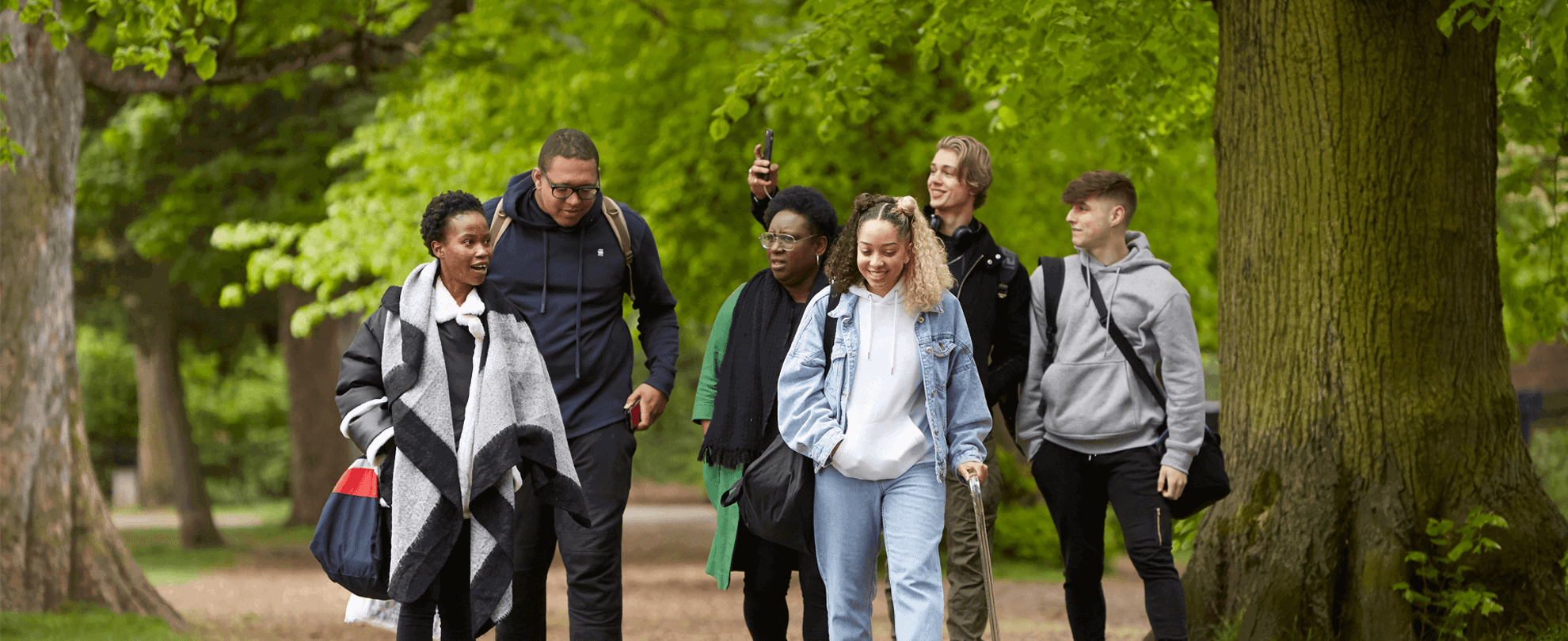 A group of six young people talking and smiling together while walking through the woods.