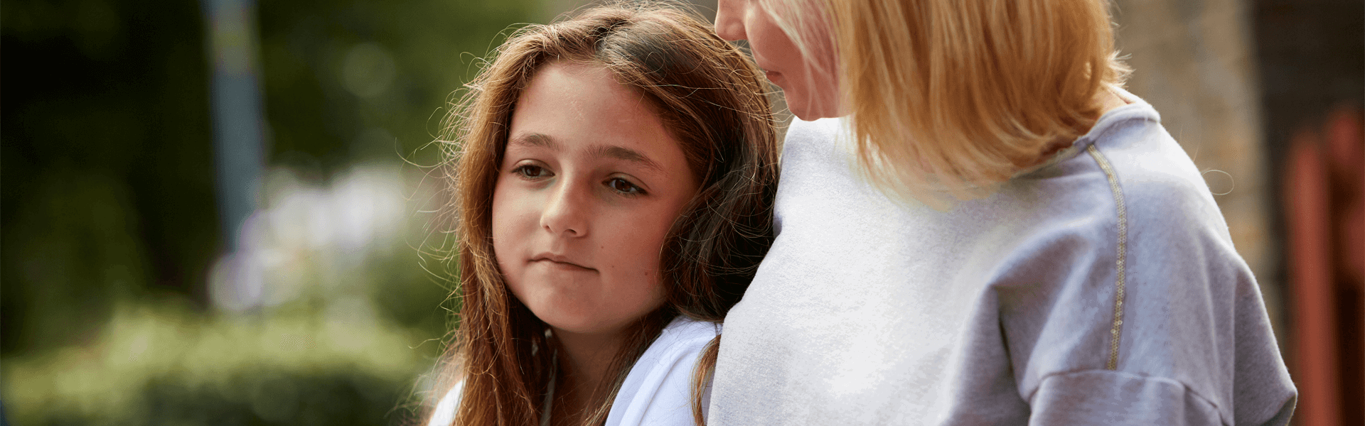 A lady comforts a young girl outside by sitting putting her arm around her