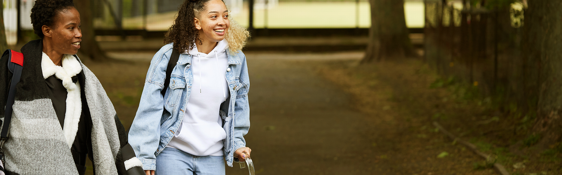 A girl with a crutch and an adult walking in the park.