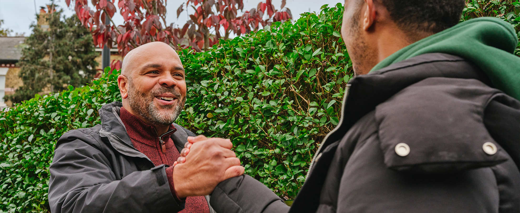A young Black man grasping hands with an older Black man on the street. They are both smiling.