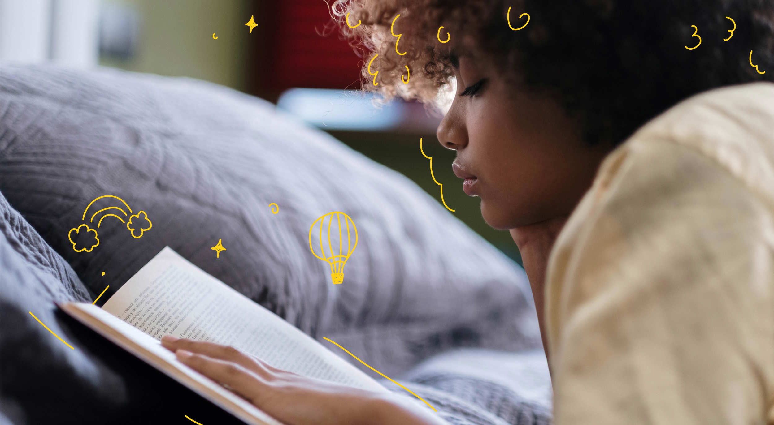 A young person reading a book lying on their front in bed.