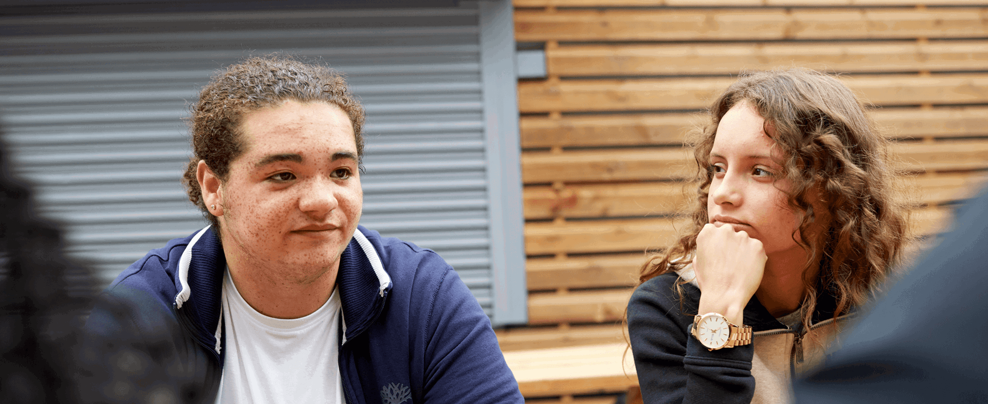 a girl with curly hair and a hand on her chin looking at a boy wearing blue jacket and a white shirt and  looks worried