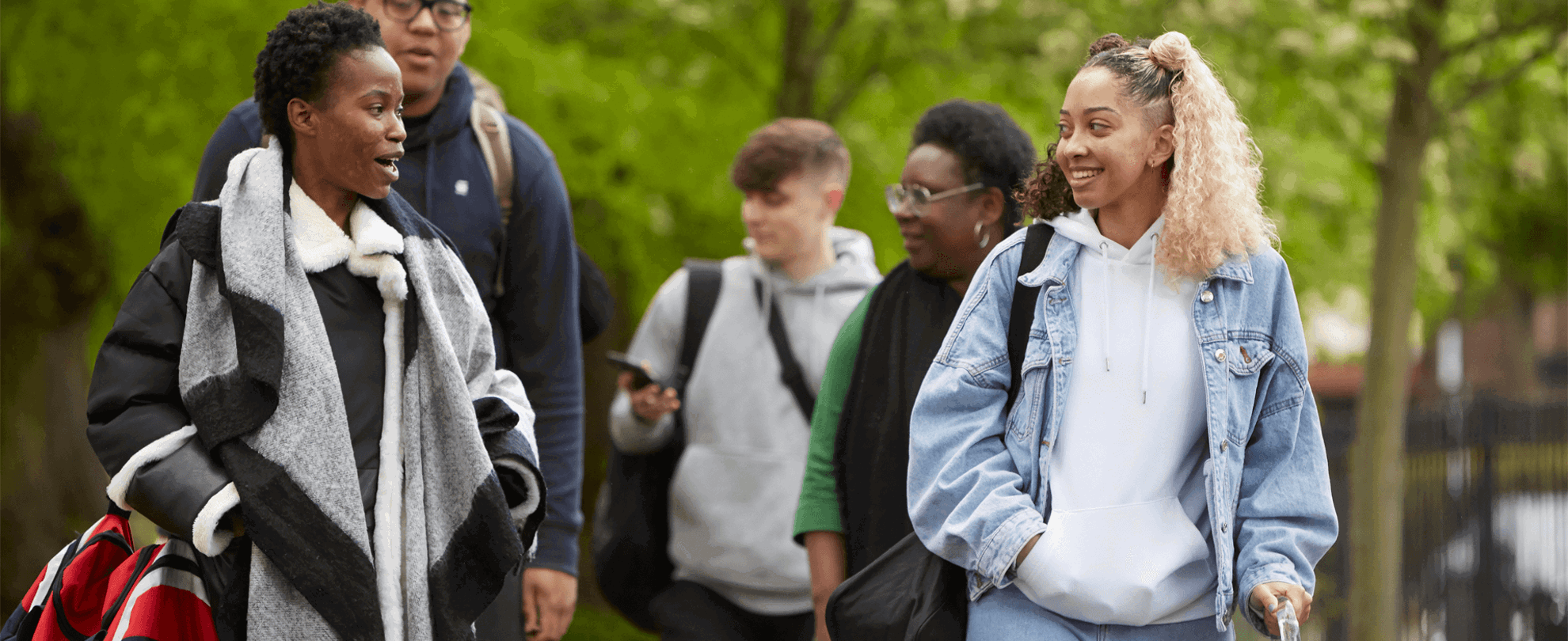 wide-shot-of-five-young-people-talking-and-smiling-while-walking-in-a-park-with-trees
