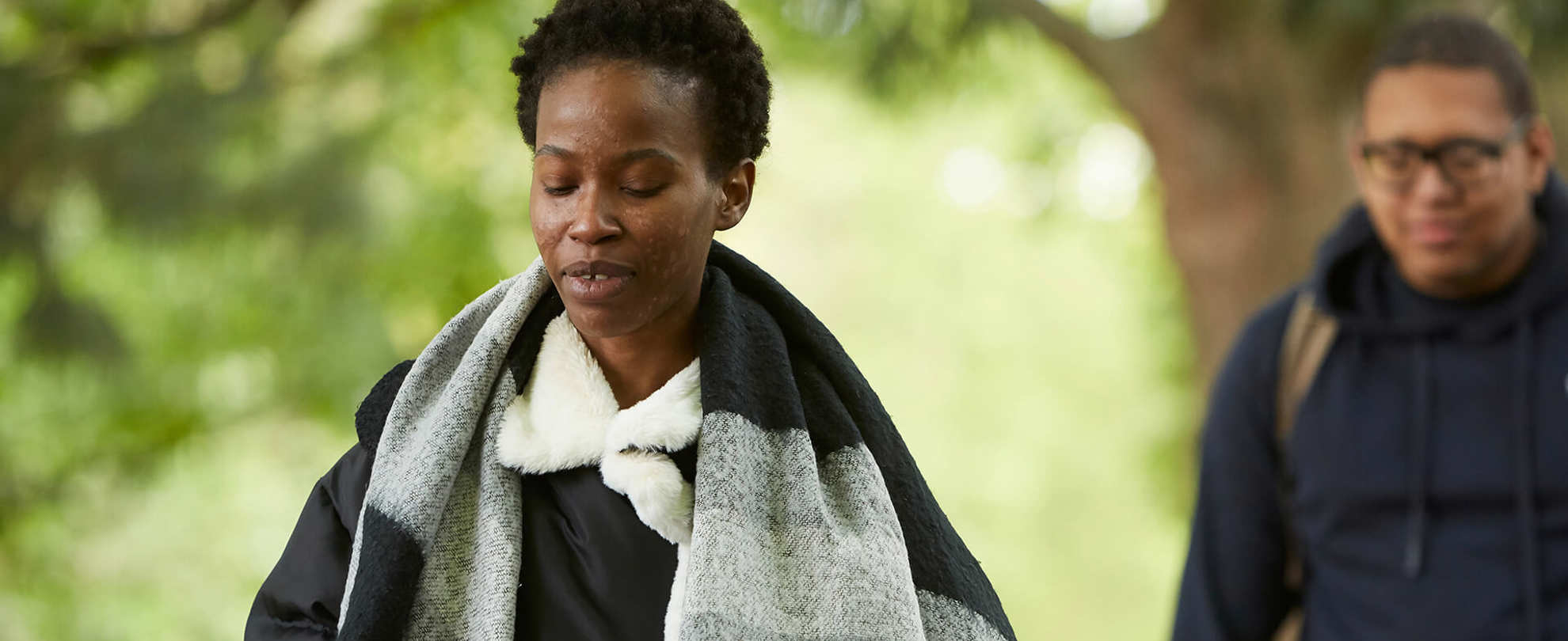 A young woman walking in a park with a friend behind her.