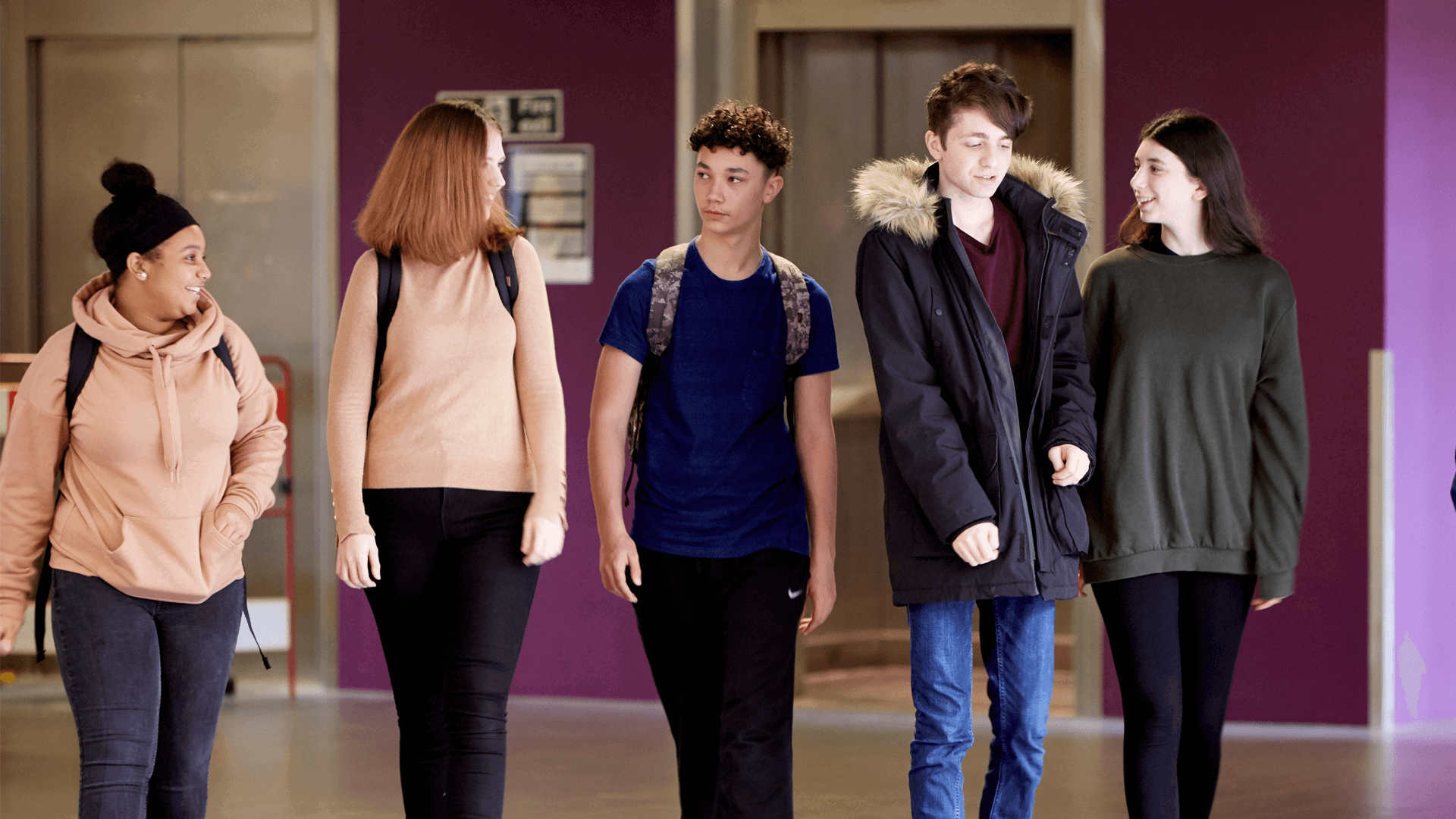 wide shot of five students wearing backpacks walking and talking inside the campus