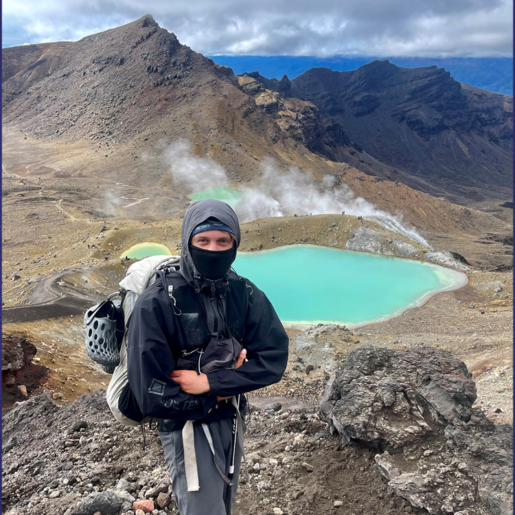 Charlie standing in front of a blue lake in the mountains.