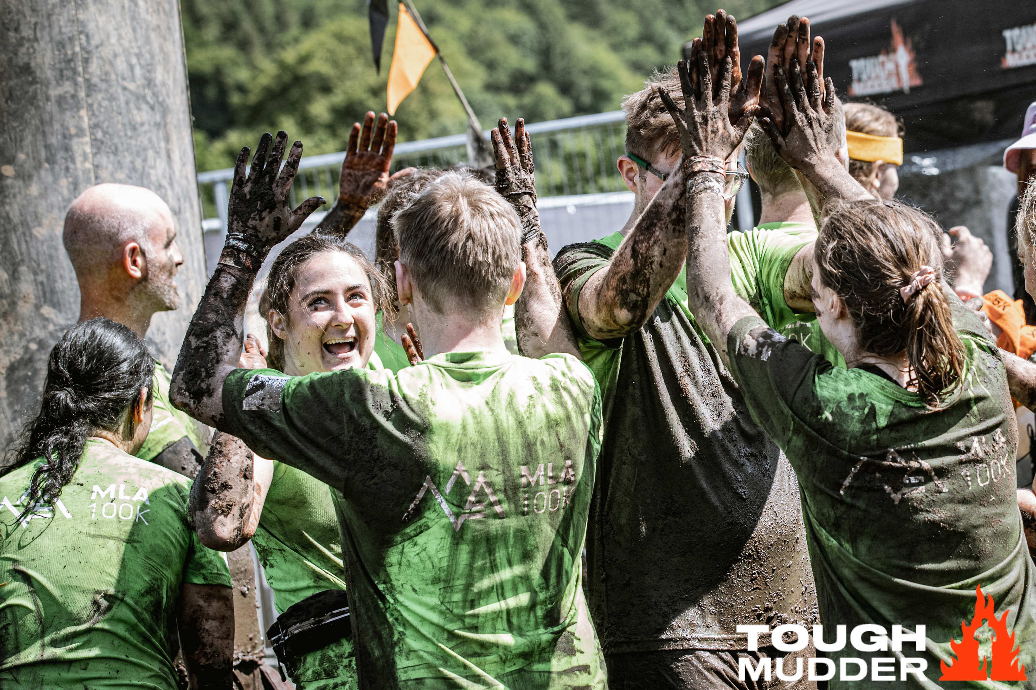 Tough Mudder participants cheering and hi-fiving, covered in mud