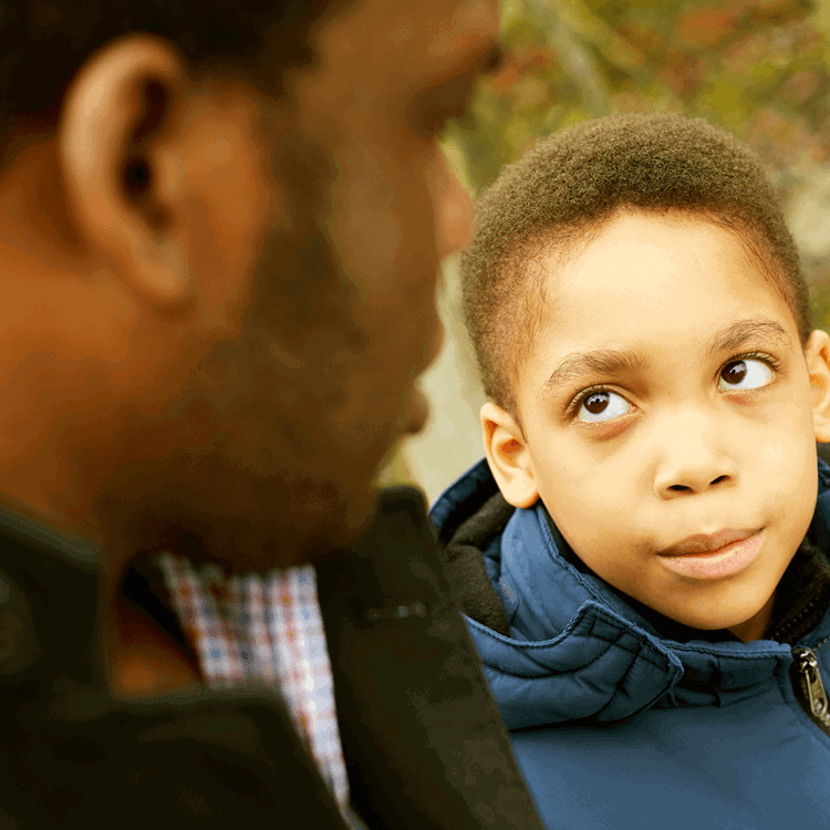A child sat next to his father and looking up to him.