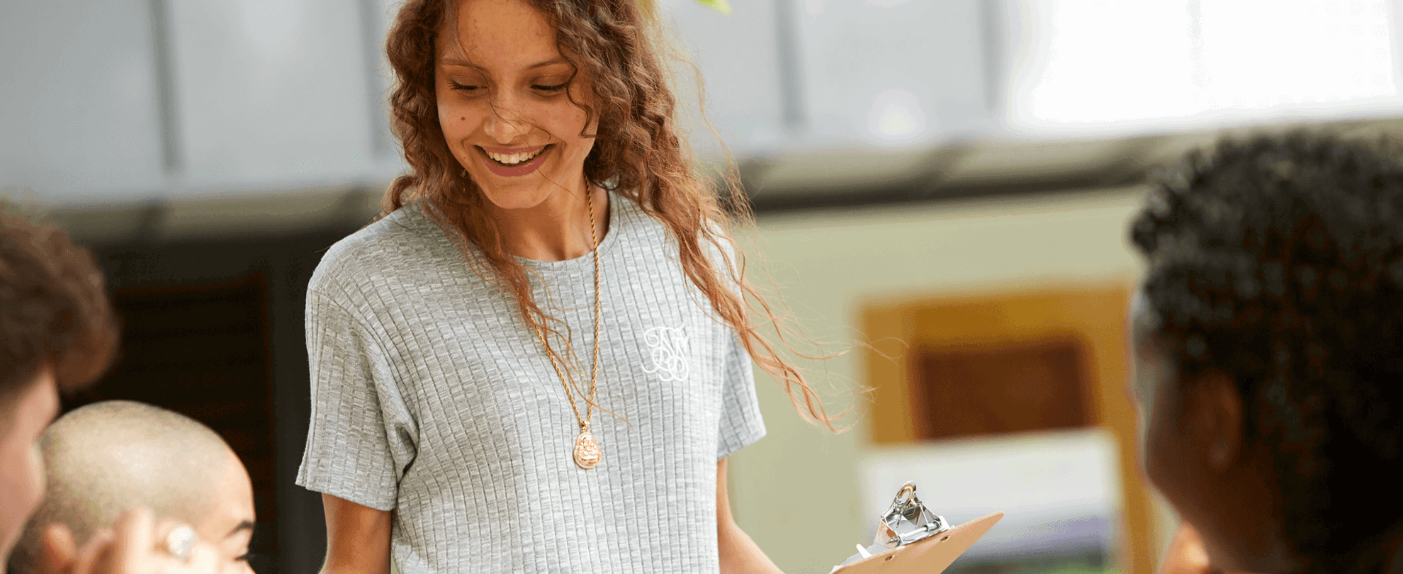 medium shot of a girl with long curly hair smiling while holding a leaflet and talking to young people in campus