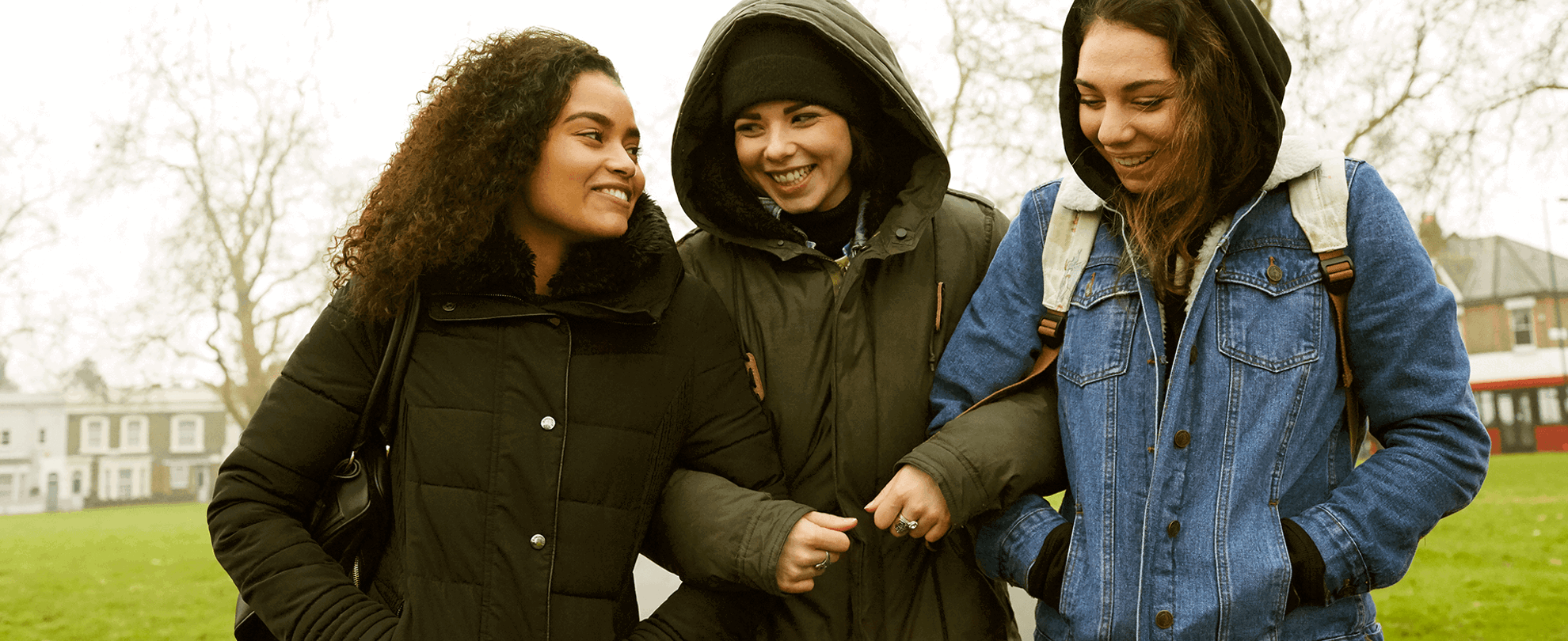 Three young people linking arms and walking through a park together.
