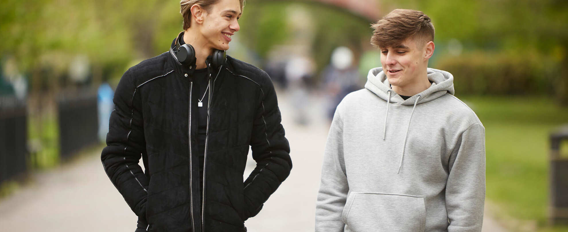 two-young-man-wearing-grey-hoodie-and-black-jacket-walking-and-laughing-on-a-street