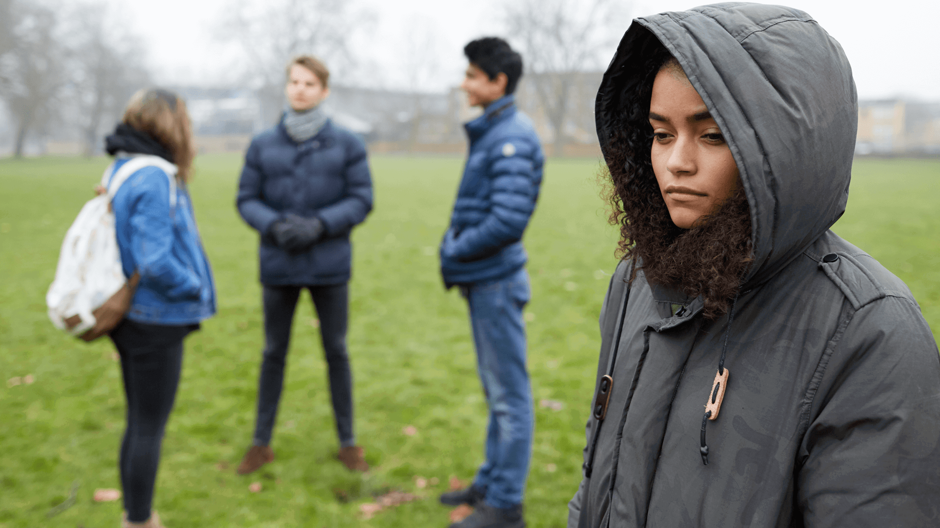 A young person stands alone feeling left out by three friends standing together.