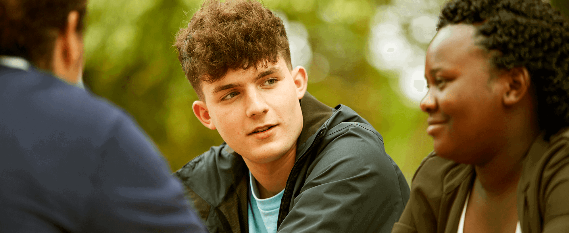 Three young people sitting together in a park.
