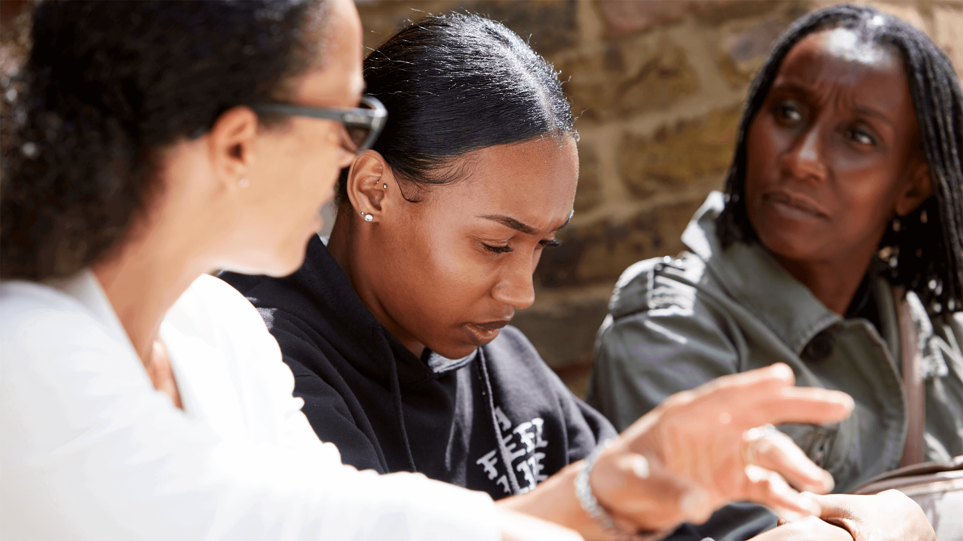 Three women sitting and talking by a wall.
