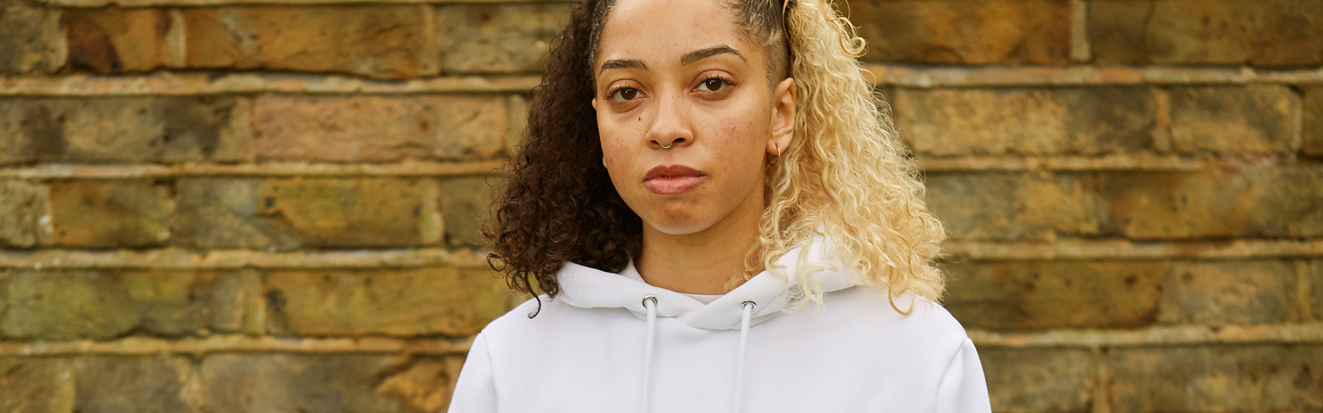 A girl staring at the camera in front of a brick wall.