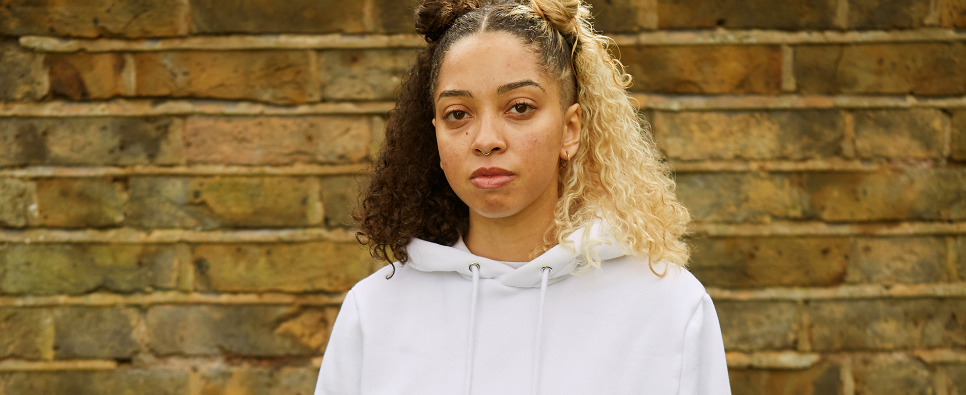 A girl staring at the camera in front of a brick wall.