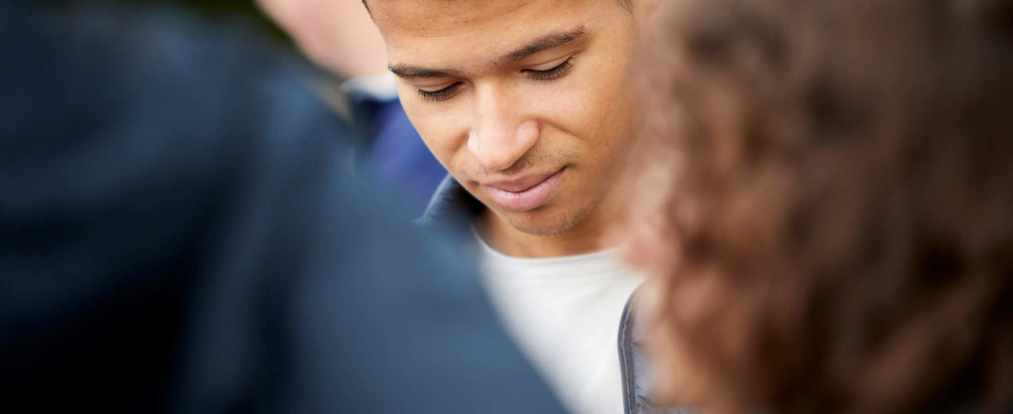 A young man stands in the centre of a group of friends with his eyes and head down.