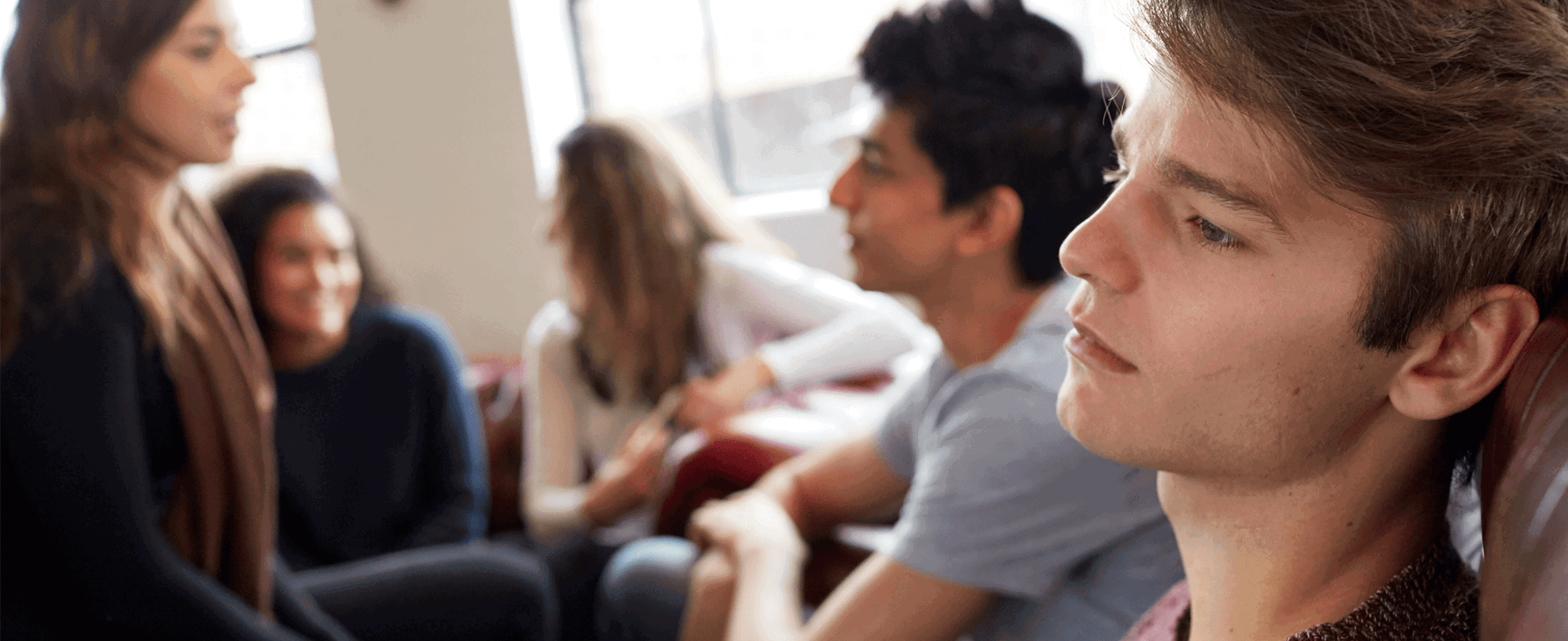A young person lost in thought while sitting with their group of friends who are talking together.