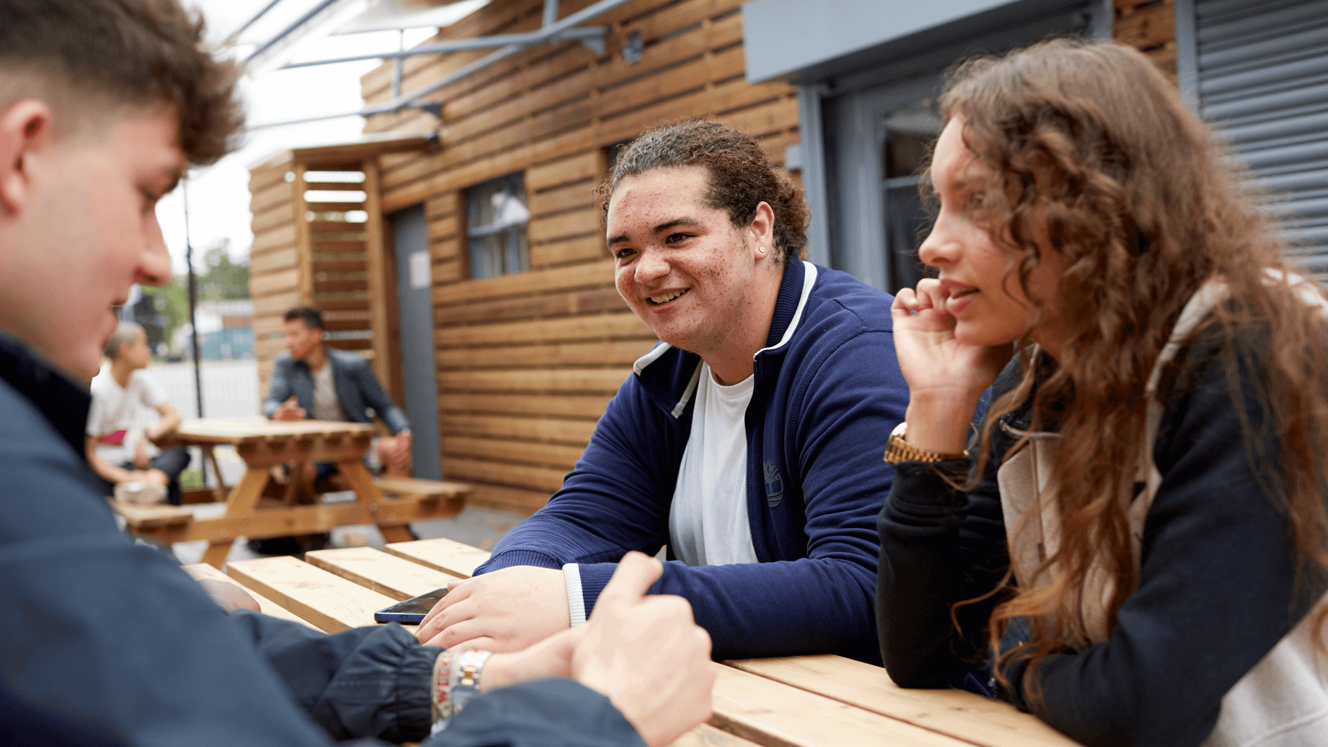 Three young people chatting and smiling while sitting at a picnic bench.