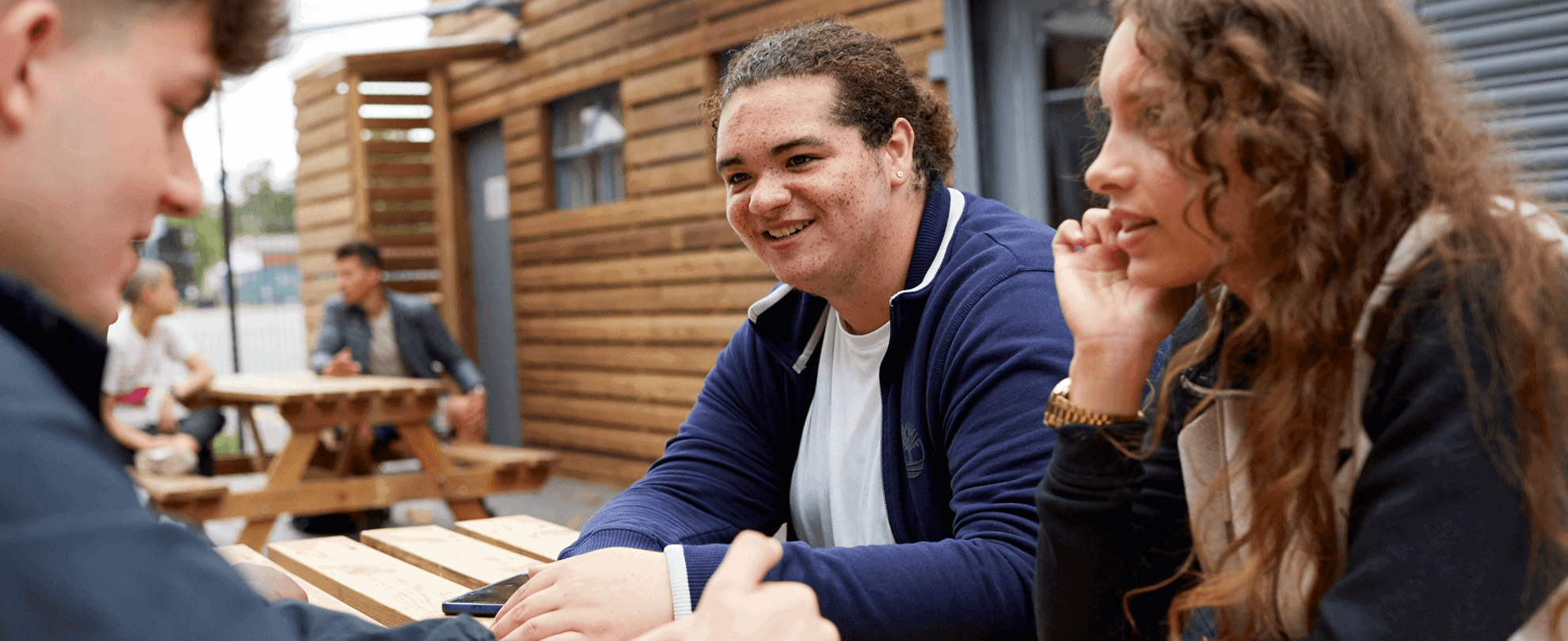 Three young people chatting and smiling while sitting at a picnic bench.