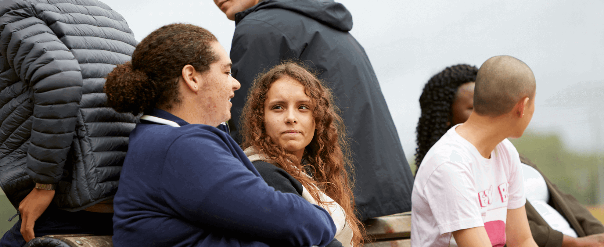 group of six young people talking and listening to one another while sitting on a bench in a park