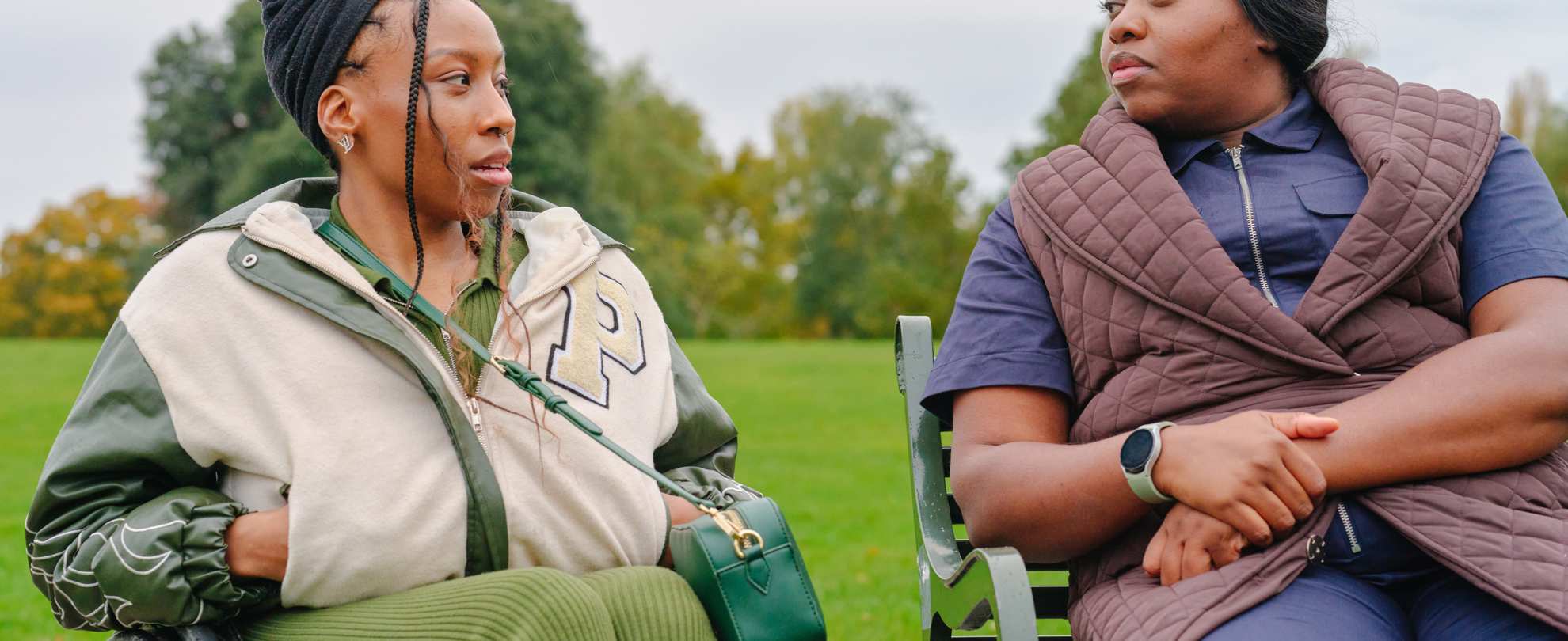 A young Black woman in a wheelchair and an older Black woman sitting on a bench in the park. They are talking about something serious.