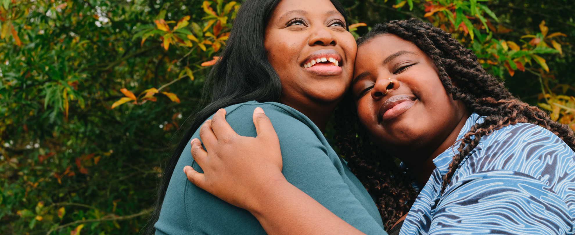 A young Black woman hugging an older Black woman in the park on a bench. They are both smiling.
