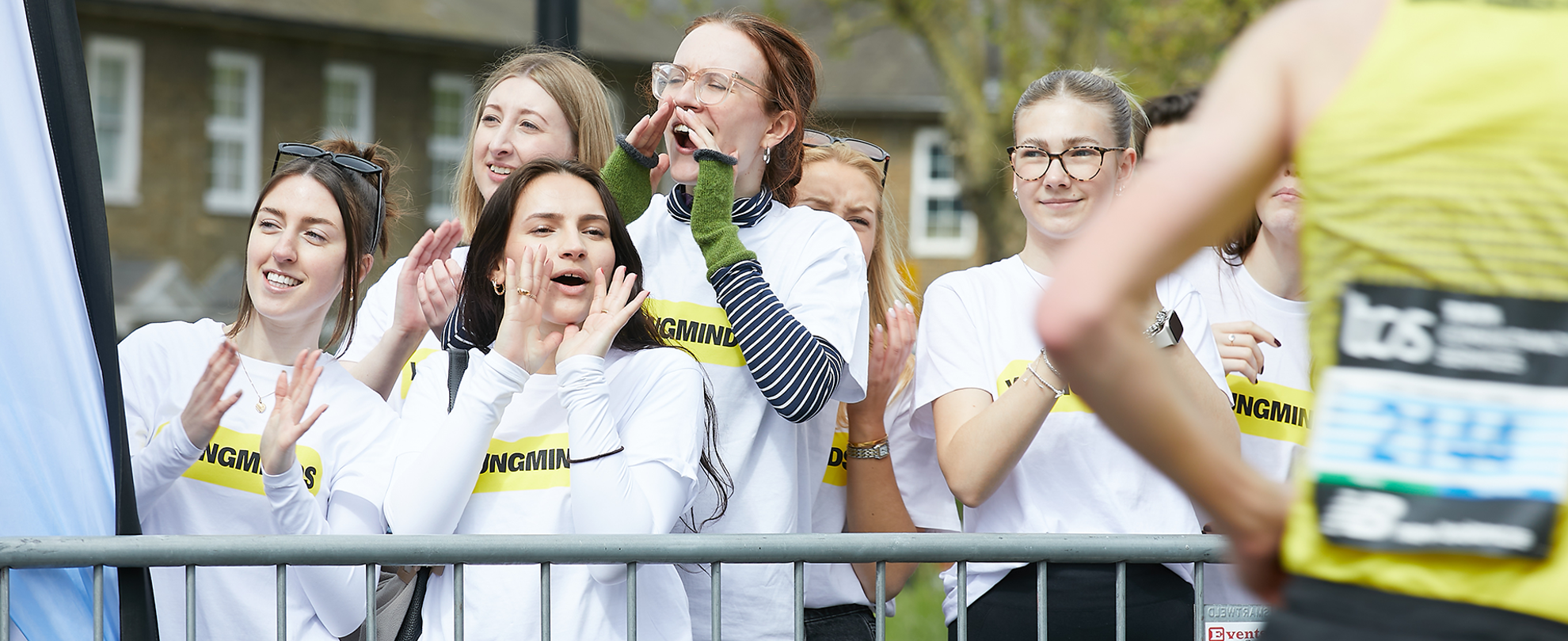 YoungMinds staff cheering marathon runners on from the side line in YoungMinds t-shirts and with YoungMinds banners.