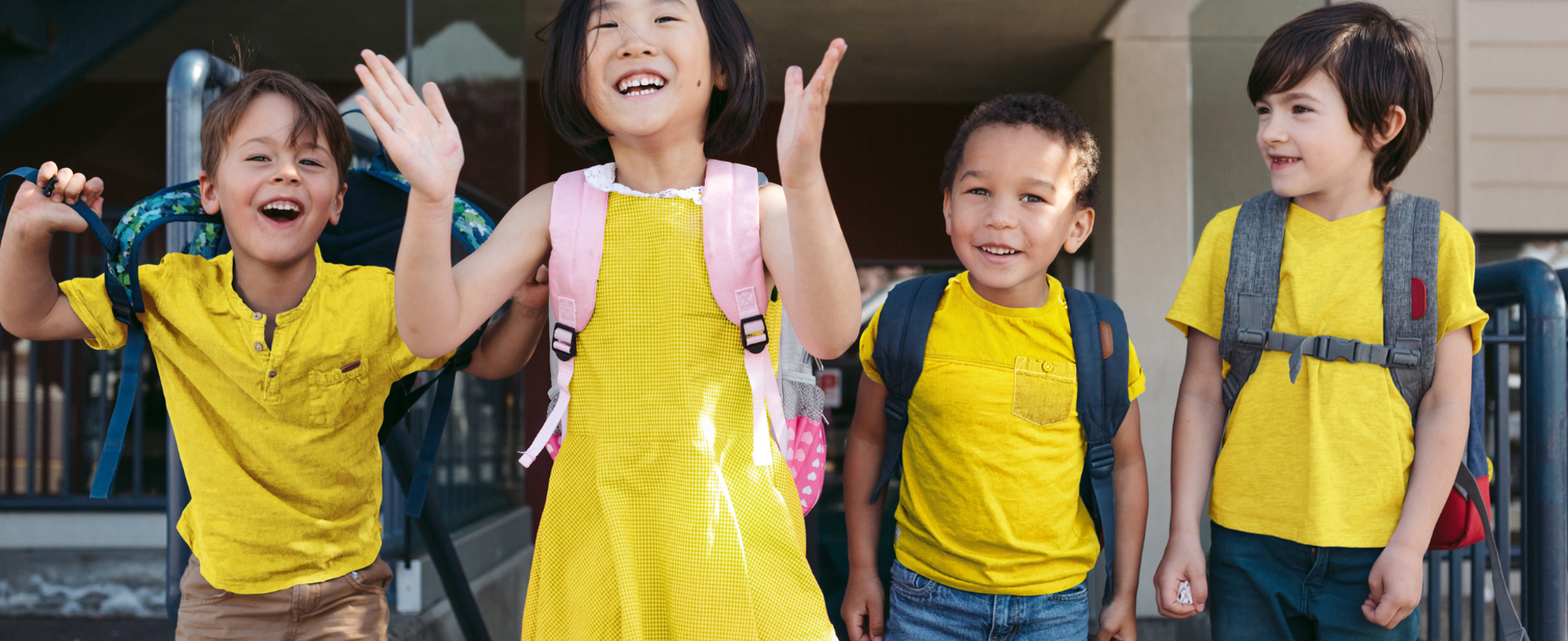 A group of school children, smiling and jumping and in bright yellow clothes.