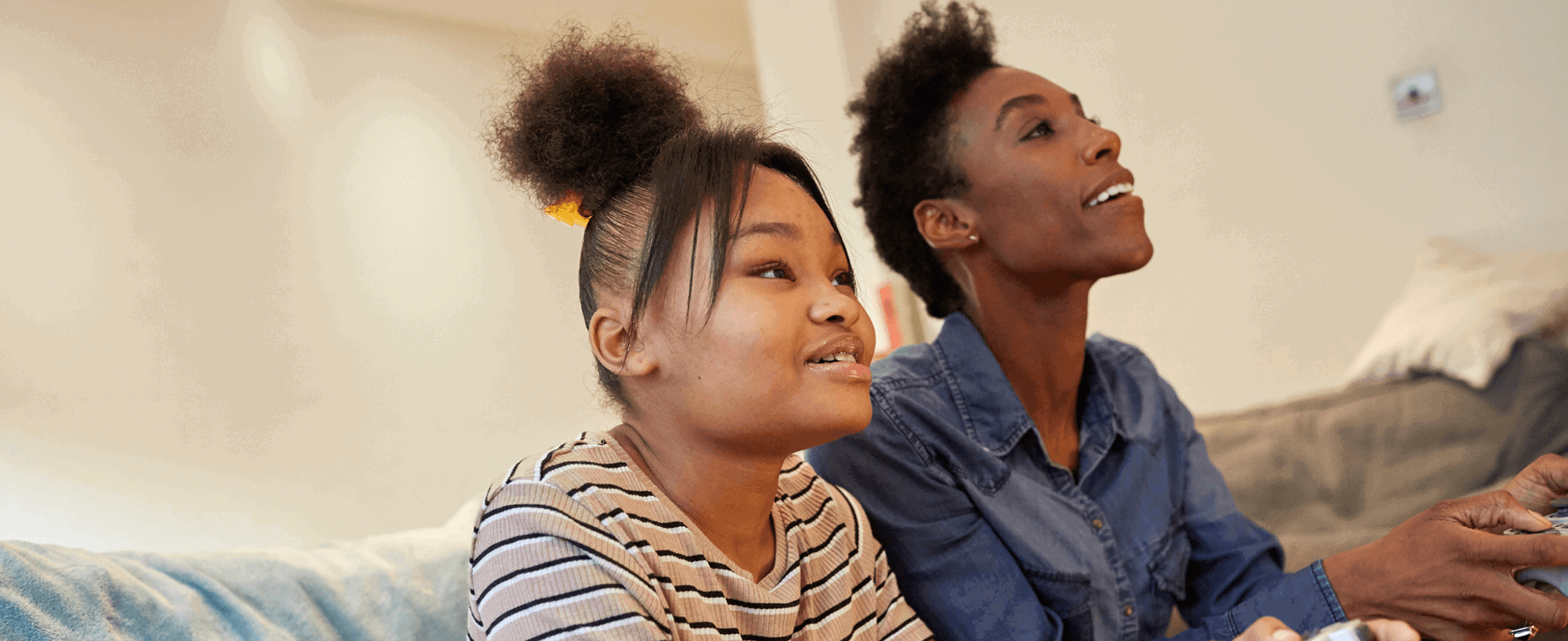A mother and daughter playing video games together happily on the sofa